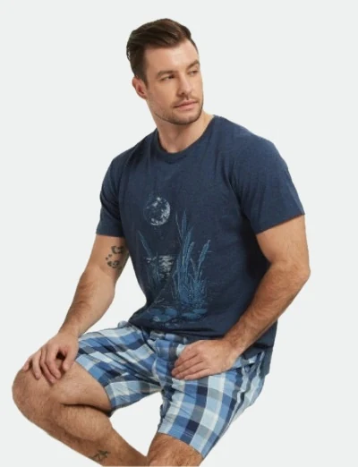 Seated man wearing a dark blue graphic T-shirt and checked shorts