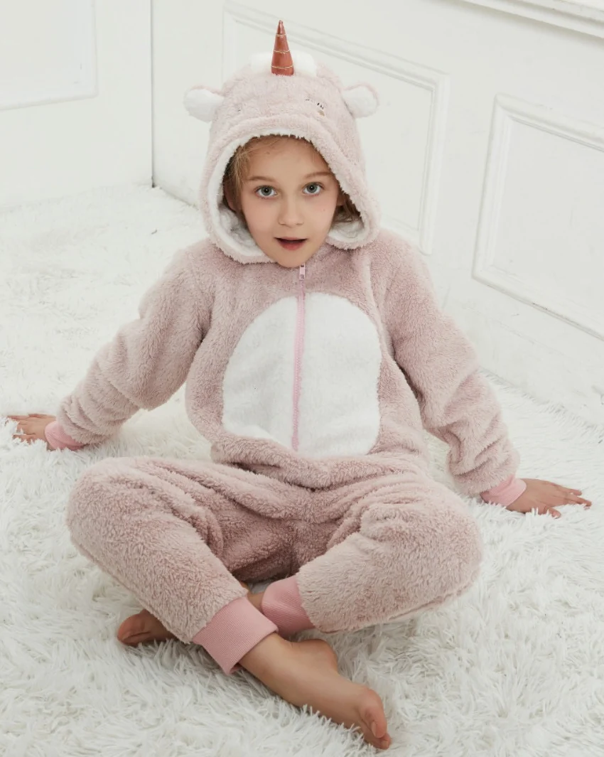 Child seated on a rug wearing a pink-and-white hooded unicorn onesie